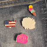 Roze Roos Emaille Pin samen met een andere bloem pin, een ijsje en Amerika emaille pin op een ondergrond van spijkerstof 