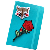 Wasbeer Racoon Strijk Embleem Patch samen met een roos strijk patch op de voorzijde van een blauwe agenda