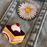 Margriet Madeliefje Met Geel Hartje Emaille Pin samen met een emaille pin van een gebakje