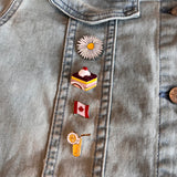 Margriet Madeliefje Met Geel Hartje Emaille Pin samen met drie andere emaille pins op een spijkerjasje