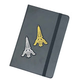 Goudkleurige Eiffeltoren Strijk Patch  samen met de zilverkleurige versie op de voorzijde van een zwarte agenda