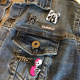 Pin Van Wit Met Roze Doodskop Met Skelet samen met vier andere pins op een blauw spijkerjasje