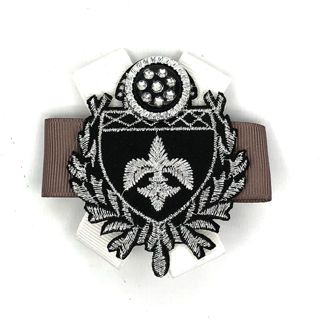 Een broche patch van een zwart met zilver kleurig embleem en sierknoop op een beige en wit gekruist lint 