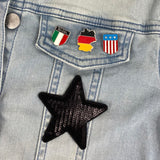 Bondsrepubliek Duitsland Vlag Emaille Pin samen met een pin van Amerika en Italië en een zwarte paillette strijk patch op een achtergrond van blauwe spijkerstof 