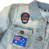 Closeup van een blauwe sigaar skull patch en een Vlag patch van Nieuw Zeeland samen op een lichtblauwe spijkerstof jas