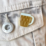 Een goudkleurige emaille pin van een bierglas / bierpul met witte schuimkraag op het borstzakje van een licht spijkerjasje v