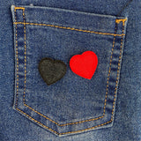 Close up van een Klein zwart Hartje Met zwart Randje Strijk Embleem Patch Applicatie samen met het zelfde hartje in het rood op de achterzak van een blauwe spijkerbroek