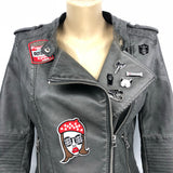 Een patch van een vrouwen hoofd met rode baret en zonnebril met love tekst een patch van een motor oil blik en 6 zwart met wit of zilverkleurige pins op een donker grijs leren jasje