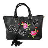 Zwarte handtas met daarop een sweet tekst patch twee roze roos patches en een bladmotief patch op een zwarte handtas