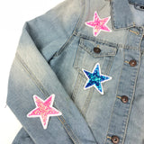 Close-up van twee roze en een blauwe fonkelende paillette ster patches op een lichtblauwe spijker jas