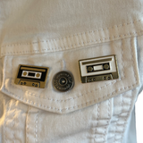 Cassette Tape Bandje Emaille Pin Vintage Zwart samen met de witte variant op een wit spijkerjasje