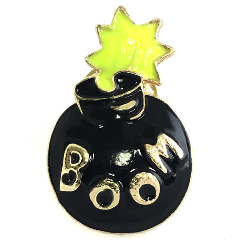 Zwarte pin van een ronde bom met lontje dat is aangestoken op de bin staat in goudkleurige letters het woord BOOM