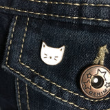 Pin van een witte poezenkop op de klep van een borstzakje van een spijkerjasjeWitte Poes Kat Emaille Pin op een achtergrond van donkerblauwe spijkerstof