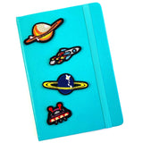 Kleine UFO Strijk Embleem Patch samen met drie andere ruimtevaart strijk patches op de voorkant van een blauwe agenda