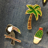 een toekan pin een palmboom pin en een cactus in pot pin op een zwarte achtergrond