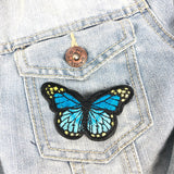 Close-up vn een blauwe vlinder patch met zwarte rand op een borstzakje van een lichtblauw spijkerjasje