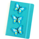 Drie Lichtblauwe Vlinder Strijk Patches op de voorzijde van een blauwe agenda
