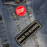 Klein rood verkeersbord strijk patch met witte tekst Stop samen met een zwart witte back to school tekst strijk patch op een ondergrond van blauwe spijkerstof